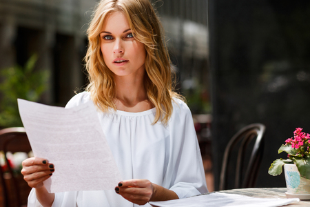 Attractive young business woman sitting in cafe and holding documents in handsの写真素材