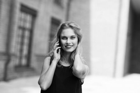 Black-and-white romantic portrait of beautiful smiling young girl with phone, portrait outdoors against the buildingの写真素材
