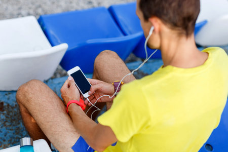 Young athlete listening music with phone in his hand sitting on stadium