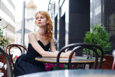 young woman in black dress at table in cafes on streetの写真素材
