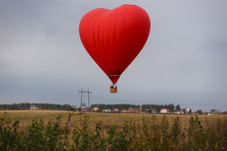 Red hot air balloon in the form of heart rises upの写真素材