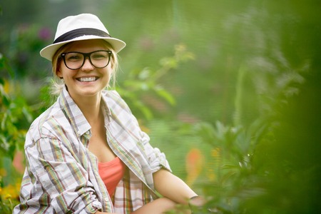 Portrait of caucasian smiling girl caring for plants in garden and looking at cameraの写真素材