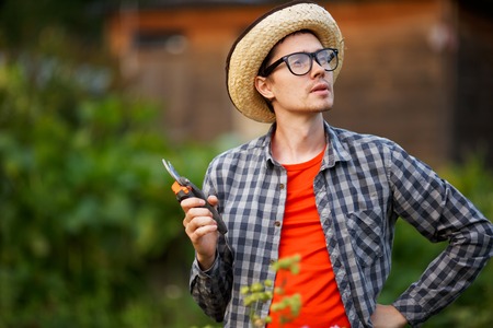 Gardener young man in hat and glasses holding pruning sheersの写真素材