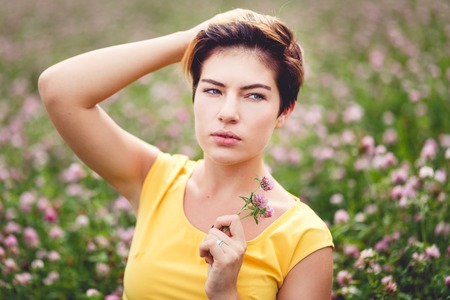 Closeup portrait of beautiful woman in field with flower in handの写真素材