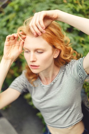 Ginger girl with curly hair in short top on street at green plant, tinted photoの写真素材