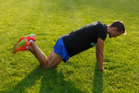 Young man in sports clothes training in park on green grass on summer warm day