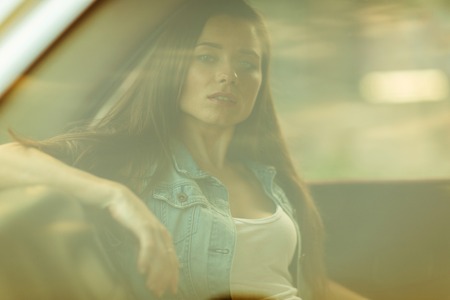 Brunette with long hair sitting in car behind closed window, tinted photoの写真素材