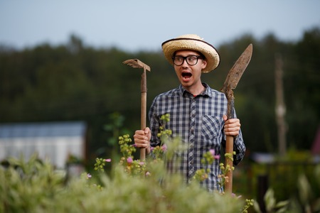 Funny expressive portrait of farmer man with shovel and rake screaming in horror at the farm workの写真素材