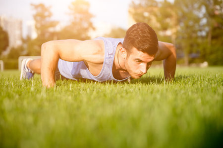 Strong athletic caucasian man doing exercises outdoors. Image with lens flare effect