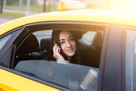 Beautiful brunette with long hair talking on phone sitting in yellow taxi in afternoonの写真素材