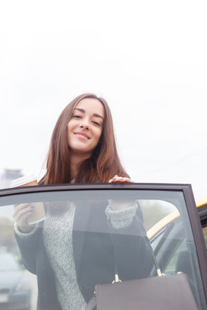 Beautiful young brunette standing at open door of car