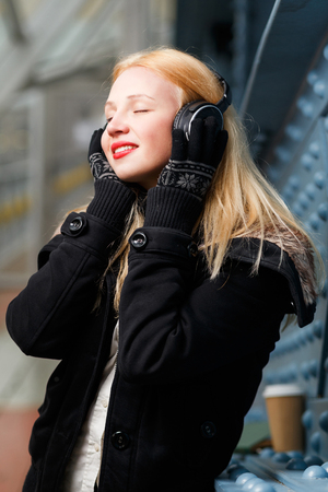 Beautiful young woman enjoying listening music with headphones standing at blue wall indoorsの写真素材