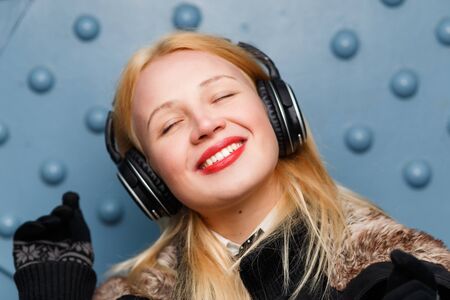 Beautiful ginger girl in black mittens and headphones enjoying listening musicの写真素材