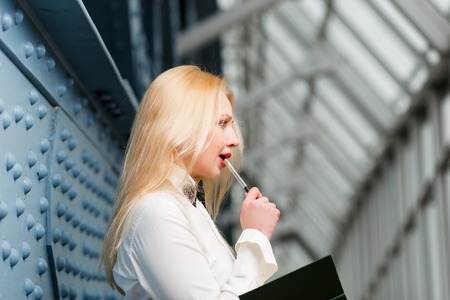Thoughtful ginger woman with red lips holding pen and note-book in long corridorの写真素材