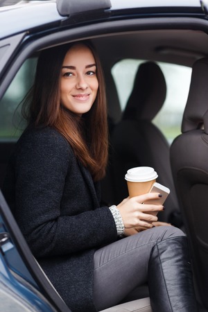 Beautiful brunette with coffee in hand sitting in carの写真素材