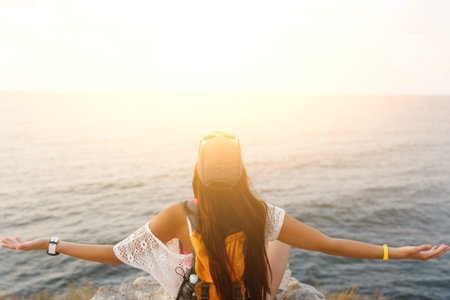 Happy freedom woman sitting and enjoying view from the cliff. Image with lens flare effect