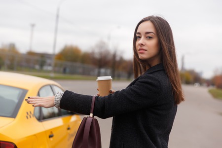 Thoughtful brunette in black coat stoping yellow taxi on streetの写真素材