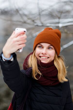 Smiling blonde girl doing selfie in winter park dayの写真素材