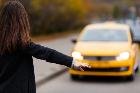 Woman with straight black hair in coat catches taxi from the road. Portrait from the back modelの写真素材