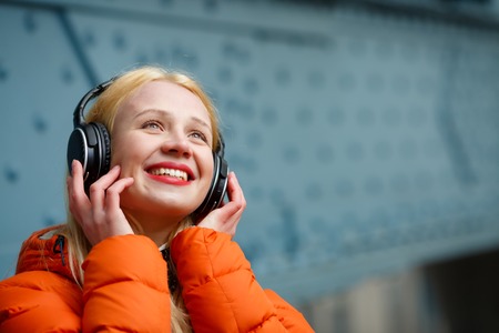 Woman in earphones listening music at blue wallの写真素材