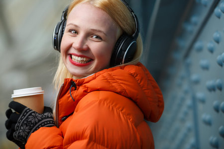 Closeup portrait of happy smiling woman with headphones and paper cup of coffee in hand. Model looking at cameraの写真素材