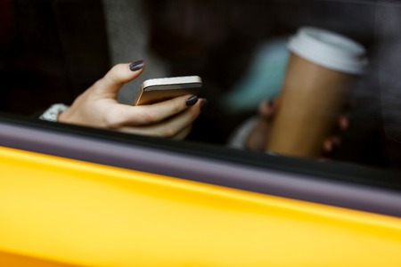 Girl with phones and coffee in hand is sitting in yellow taxiの写真素材