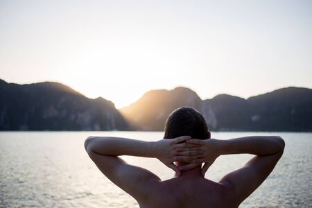 Man with hands behind head on seashoreの写真素材
