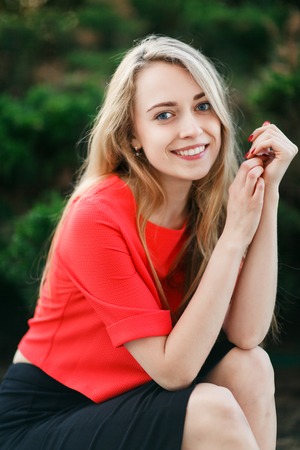 Young woman in red jacket against green bush ,blurred backgroundの写真素材