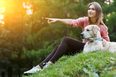 Photo of girl pointing forward next to dog on green lawnの写真素材