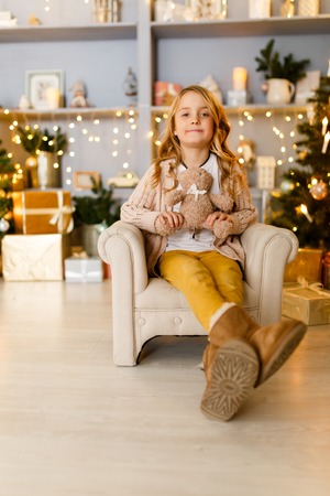 Photo of girl sitting in chair on background of Christmas decorationsの写真素材