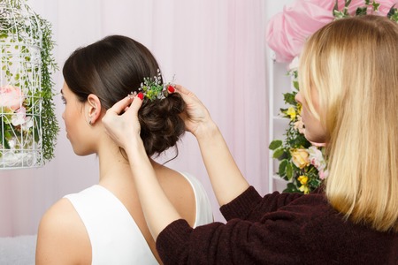 Image of woman sitting on chair and stylist adjusting hair in pink studioの写真素材