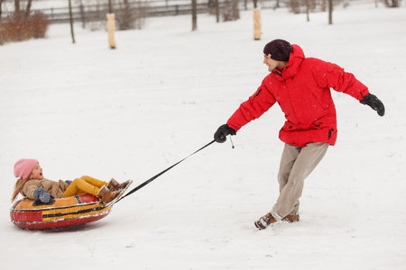 Photo of father dancing daughter on tubing in winter afternoon