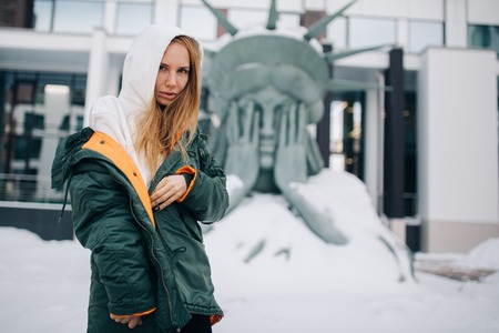 Portrait of blonde in hood and jacket against background of buildingの写真素材