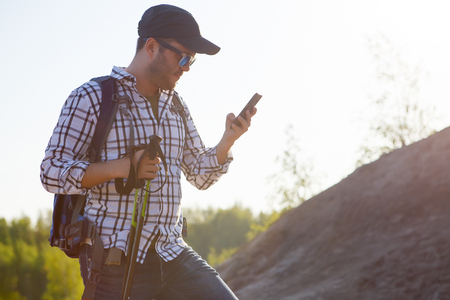 Photo of tourist man with walking sticks and telephone on mountain hillの写真素材