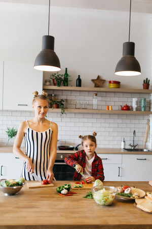 Photo of beautiful woman with her daughter cutting vegetables in kitchenの写真素材