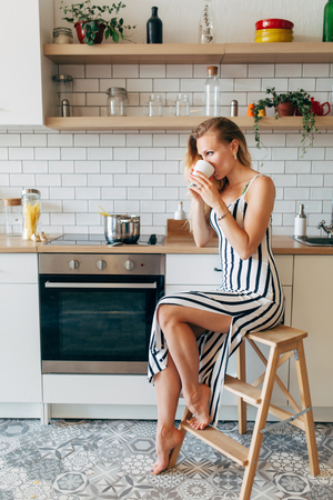 Photo of beautiful woman in long striped dress in kitchenの写真素材