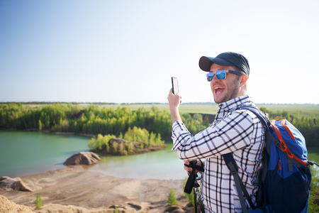 Photo of tourist man with walking sticks doing selfie on hillの写真素材