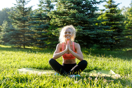Photo of young curly-haired sports woman practicing yoga on rug in parkの写真素材