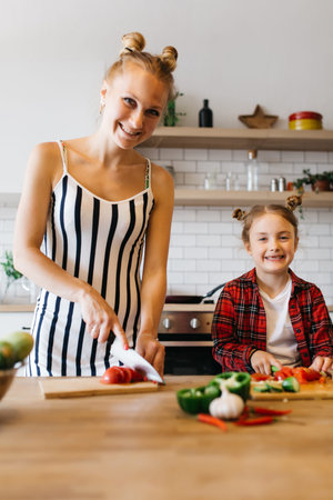 Photo of beautiful woman with her daughter cutting vegetables in kitchenの写真素材