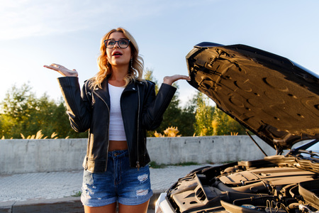Photo of frustrated woman with curly hair near broken car with open hoodの写真素材