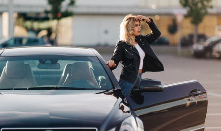 Image of young blonde at open door of black carの写真素材