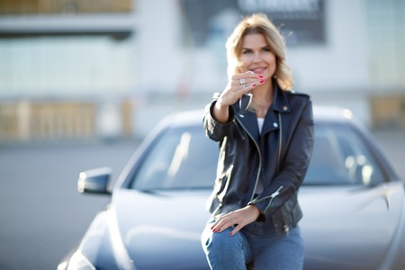 Photo of young woman with keys sitting on hood of black carの写真素材