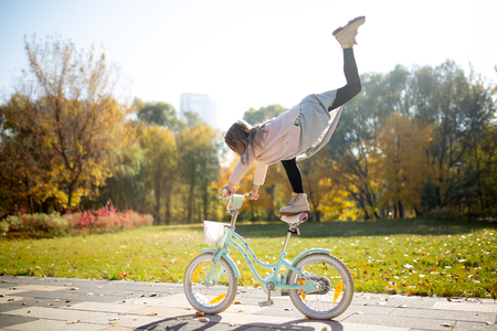Image of girl in skirt with raised leg riding bike in autumn parkの写真素材