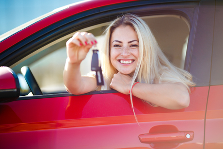 Photo of beautiful blonde woman with keys sitting in red car with open windowの写真素材