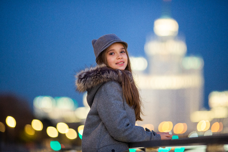 Photo of girl in gray hat and coat on waterfront on background of spots, lights, blurred backgroundの写真素材