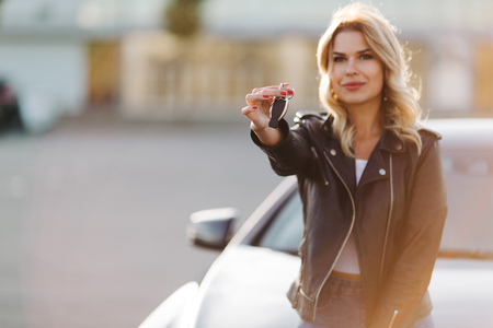 Image of young blonde girl with keys sitting on hood of black carの写真素材