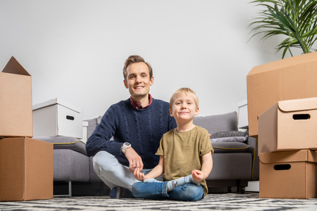 Photo of father and boy sitting on floor among cardboard boxesの写真素材