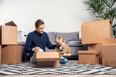 Portrait of man and boy with microscope sitting on floor among cardboard boxesの写真素材