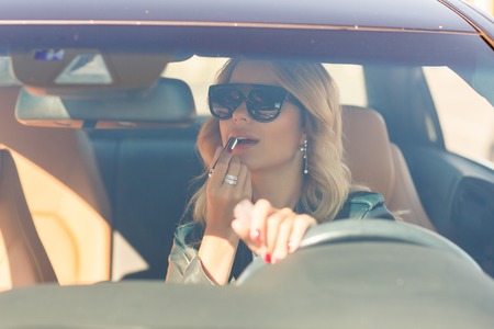 Woman with long hair painting her lips while driving in car.の写真素材