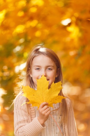 Photo of girl with leaf of maple in autumn park in afternoonの写真素材